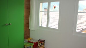 Una habitación con un armario verde, una ventana con vista al tejado y juguetes infantiles en el suelo.