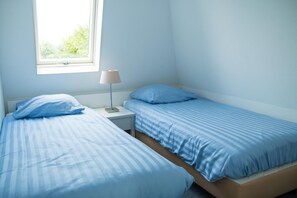 Un dormitorio con dos camas, una mesita de noche, una lámpara y un ventanal con vistas al verdor.