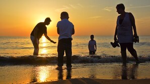 Un coucher de soleil sur la plage, avec des personnes debout dans l’eau.