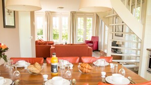 Un coin repas avec une table en bois mise pour le petit-déjeuner, des chaises orange et un escalier menant à un niveau supérieur.