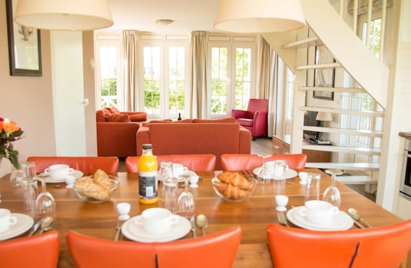 Un comedor con una mesa de madera preparada para el desayuno, sillas color naranja y una escalera que sube a un nivel superior.