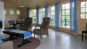 Amplia habitación con techo de madera, ventanas grandes con cortinas azules, una mesa de billar y varias sillas.