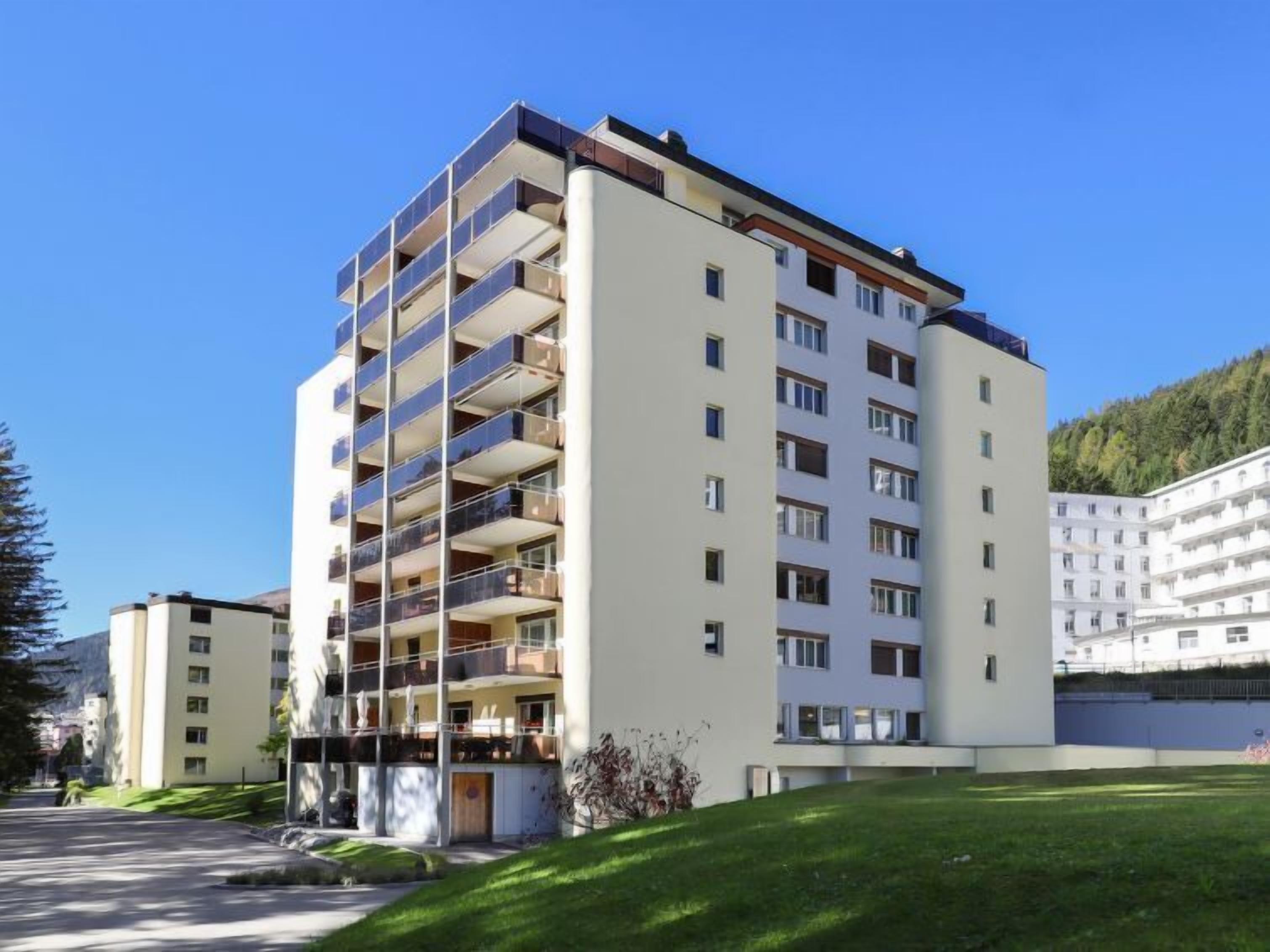 A multi-story residential building with balconies, a flat roof, and a clear sky.