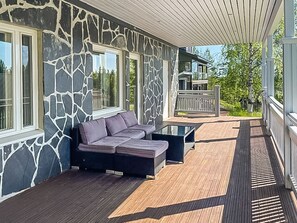 Un espacio exterior cubierto con un muro de piedra, una terraza de madera y un área de descanso con cojines.
