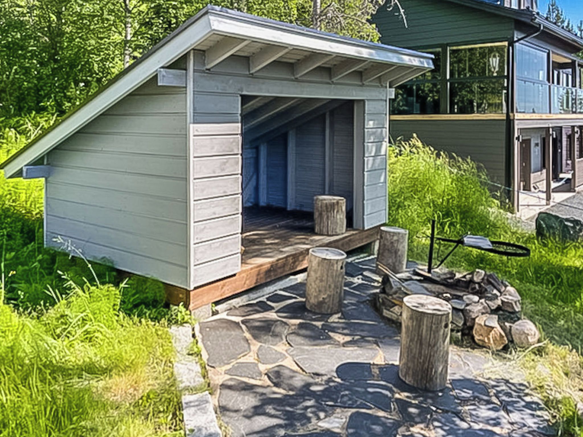A small wooden cabin with a sloped roof, a stone-paved entrance, and a fire pit with logs.