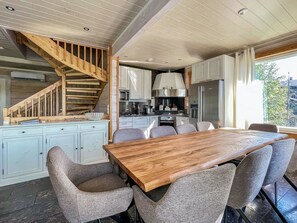 A modern kitchen with a wooden staircase, a dining area with a large table and chairs, and a view of the outdoors.
