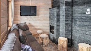 Een knus blokhutinterieur met een hoekbank, een open haard, houten krukken en een wandtelevisie.