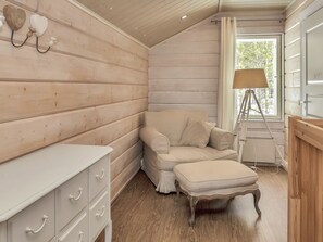 A cozy room with a wooden interior, a beige sofa, a small table with drawers, and a lamp near a window.