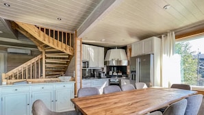 Een moderne keuken met een houten trap, witte kasten en een grote eettafel met grijze stoelen.