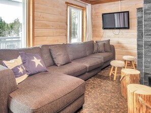 A modern log cabin interior with a sectional sofa, a flat-screen TV, and a stone fireplace.