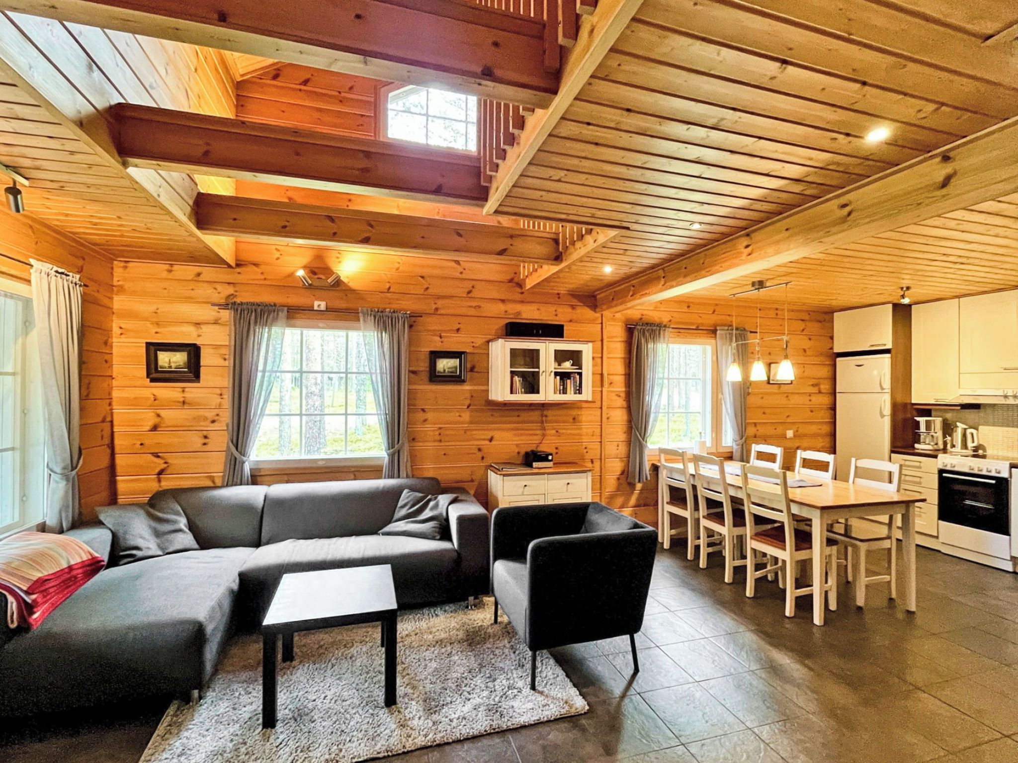 A cozy cabin interior with a sofa, dining table, chairs, and a kitchen area.