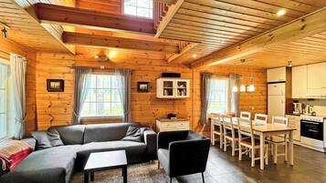 A cozy cabin interior with a sofa, dining table, chairs, and a kitchen area.
