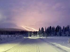 A snowy landscape with a road leading towards a brightly lit structure in the distance.