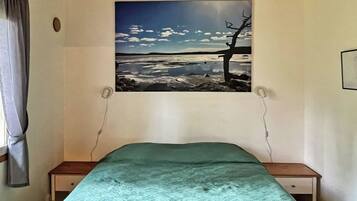 A bedroom with a bed, a window with a painting, and a wooden ceiling.