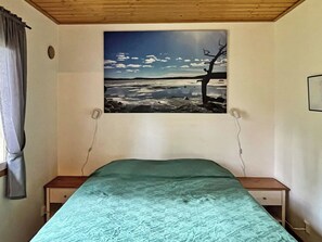 Een slaapkamer met een bed, een raam met een schilderij en een houten plafond.