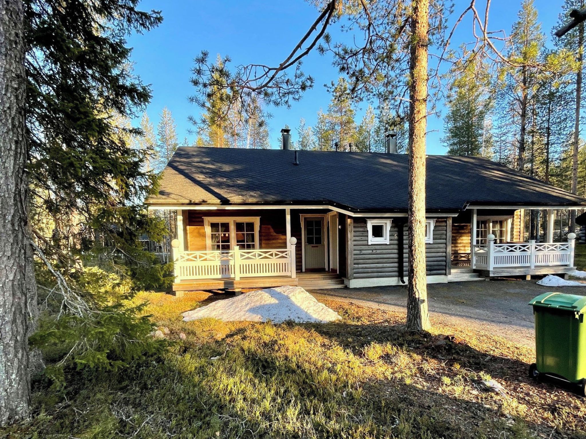 Eine zweistöckige Holzblockhütte mit Veranda, umgeben von Bäumen.