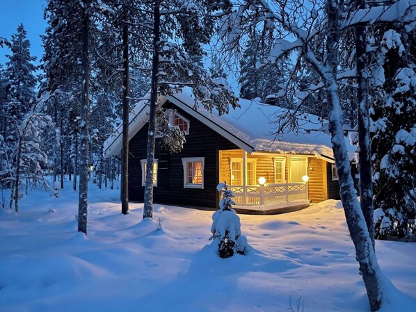 A wooden cabin with a porch, surrounded by snow-covered trees.