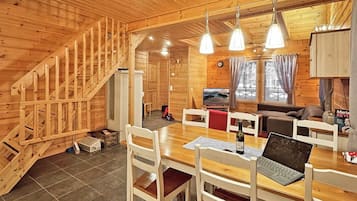 A wooden cabin interior with a dining area, a sofa, a television, and a staircase.