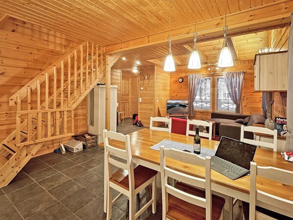 Een houten cabin met een eethoek, een bank, een televisie en een trap.