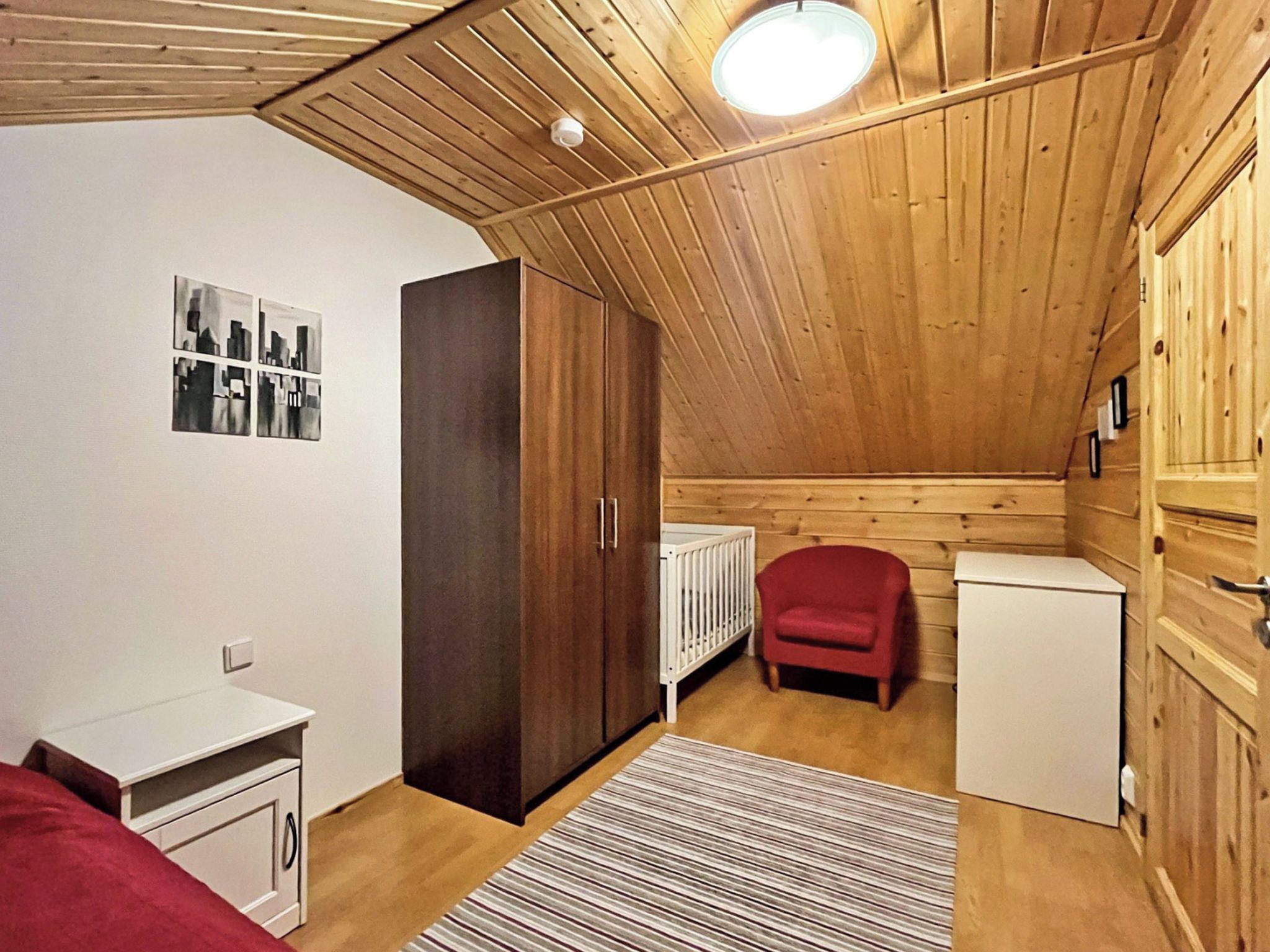 Pieni huone, jossa on kalteva katto, valkoinen patteri, punainen tuoli ja pieni valkoinen kaappi.