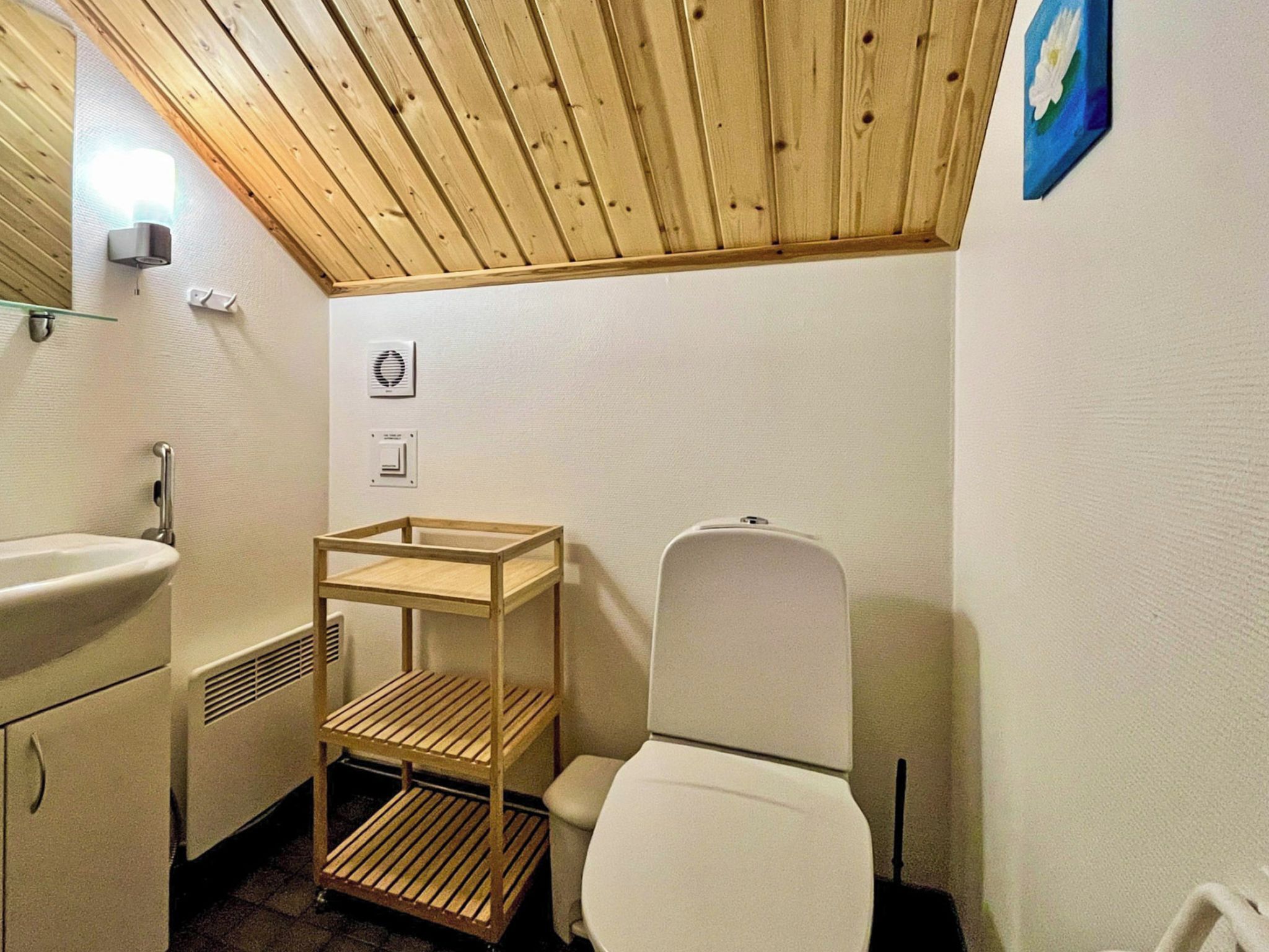 Pieni kylpyhuone, jossa on puinen katto, valkoinen wc-istuin, puinen hyllykkö ja pesuallas.