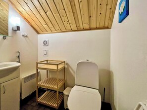 Een compacte badkamer met een houten plafond, een wit toilet, een houten plankunit en een wastafel.