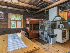 A rustic cabin interior with a wooden dining table, a bunk bed, a stone fireplace, and a kitchenette. - Rauhalinna by Interhome (Juva)