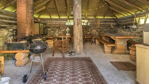 Ein rustikales Blockhaus-Interieur mit Kamin aus Stein, Holztischen und einem Grill.