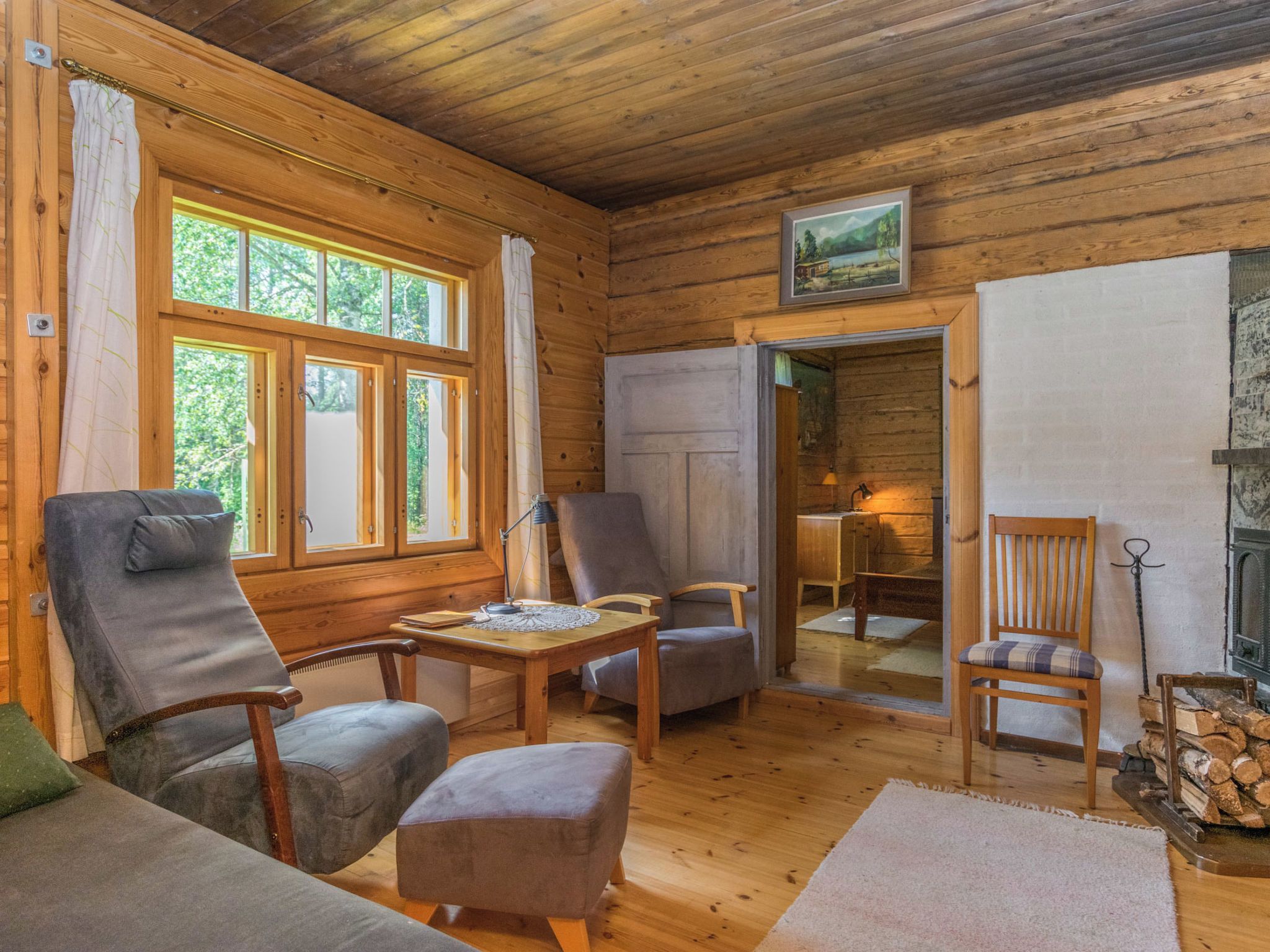 Ein gemütliches Blockhaus-Interieur mit Holzwänden, einem Esstisch, zwei Stühlen, einer Couch und einem Kamin.