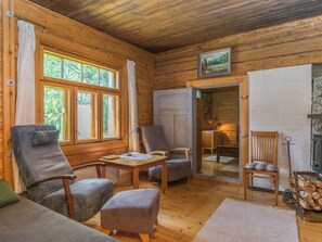 A cozy cabin interior with wooden walls, a dining table, two chairs, a sofa, and a fireplace.