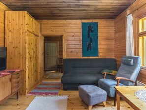 Ein Holzblockhaus-Innenraum mit einer Couch, einem Sessel, einem kleinen Tisch und einem Fernseher auf einem Schrank.