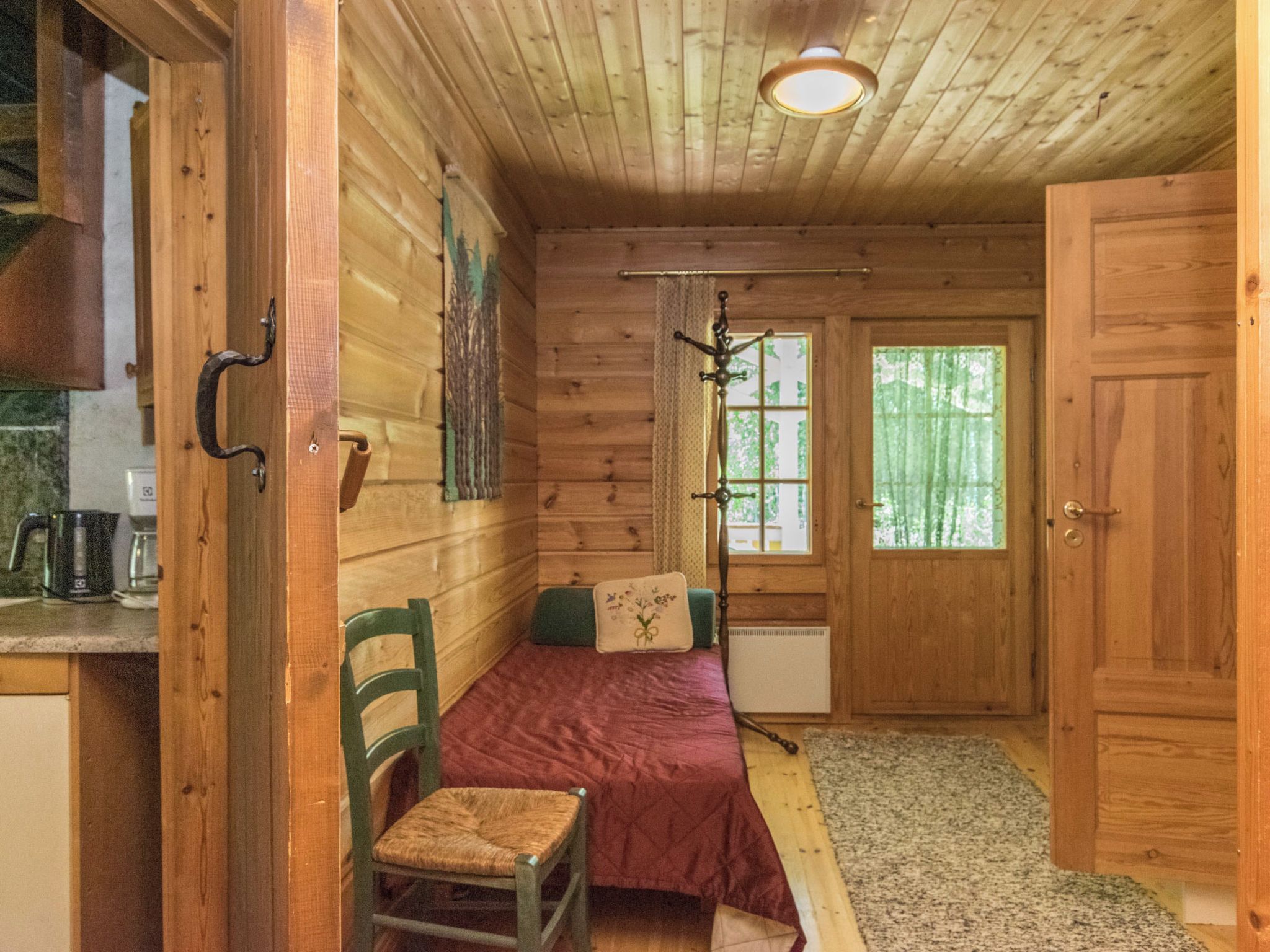 L’intérieur d’une cabane en bois, avec un lit, une chaise, une fenêtre et une porte.