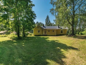 A yellow house with a tiled roof, surrounded by a grassy yard and trees. - Rauhalinna by Interhome (Juva)