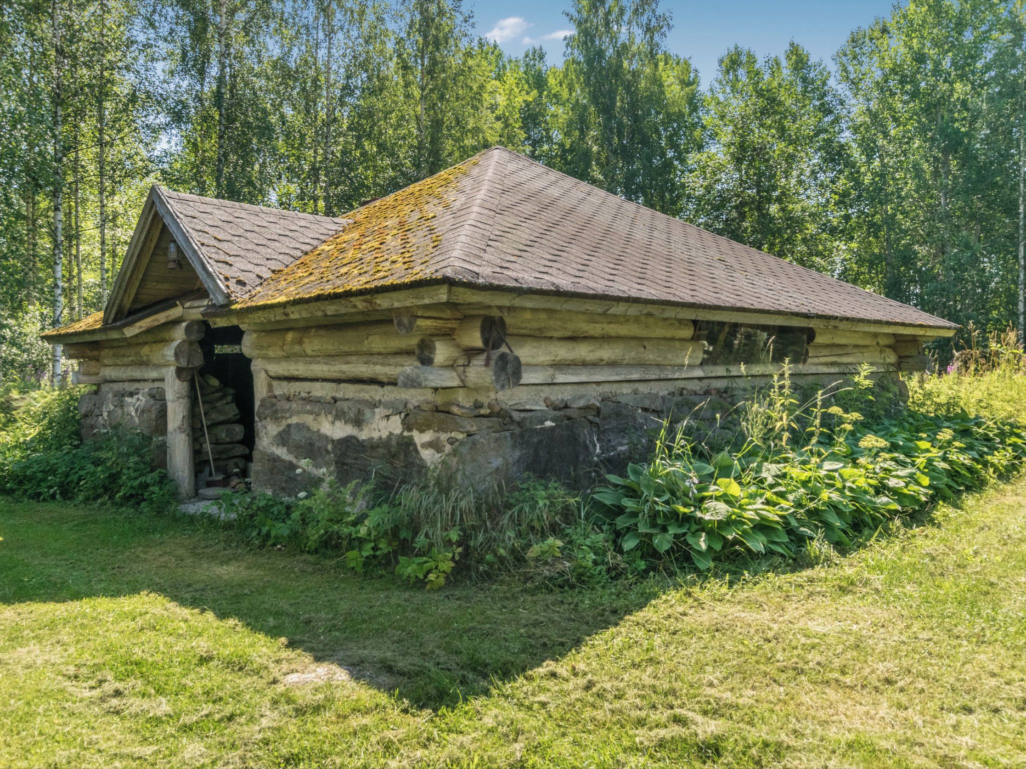 Une cabane rustique en rondins de bois, dotée d’un toit en pente, d’une cheminée et d’un petit porche.