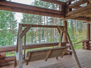 Una terraza de madera con un columpio, rodeada de un área boscosa.