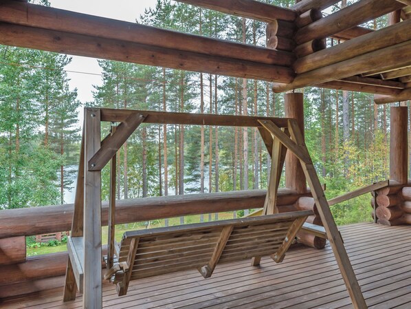 Una terraza de madera con un columpio, rodeada de un área boscosa.