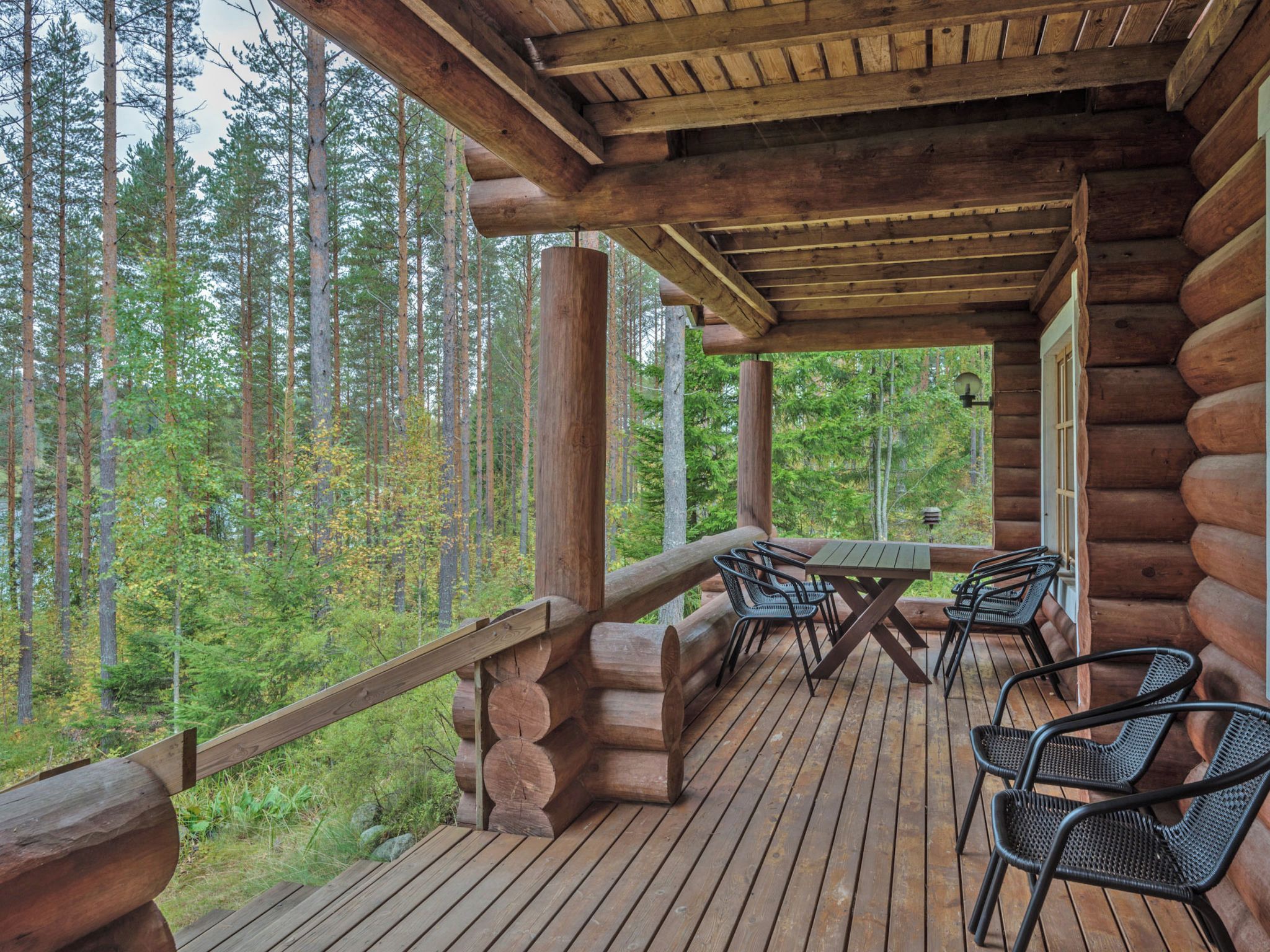 Eine Holzblockhütte mit einer Holzdiele, Sitzgelegenheiten im Freien und Blick auf den Wald.