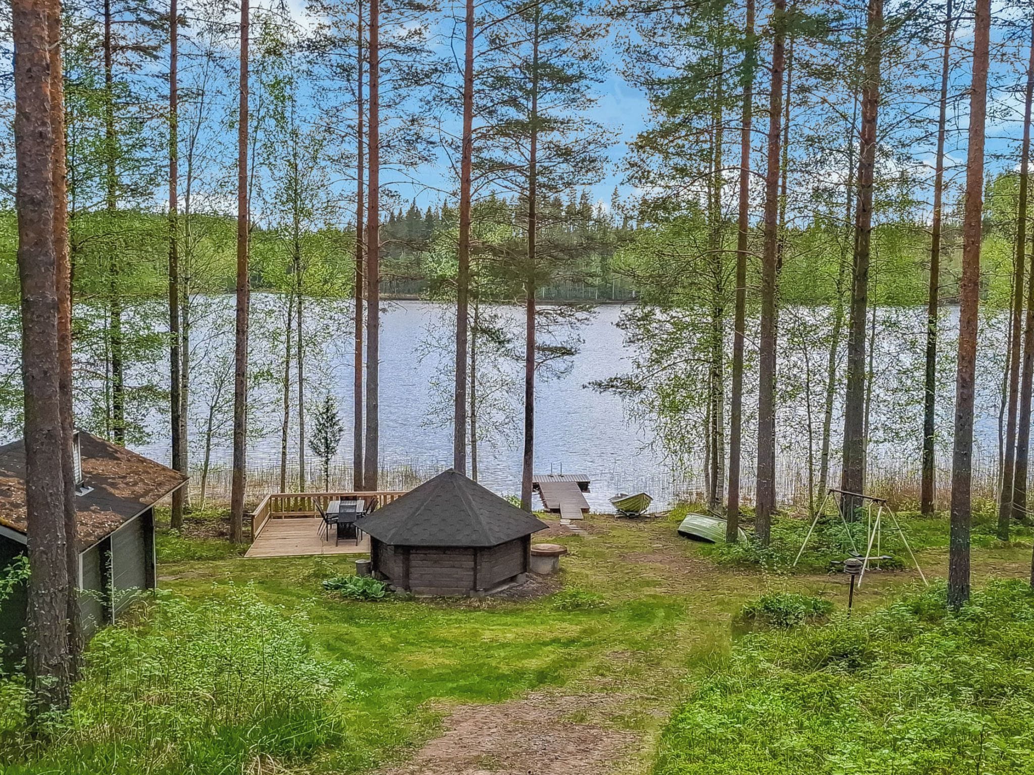 Een chalet met terras en een kleine schuur, omgeven door hoge bomen en een meer.