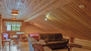 L’intérieur d’une cabane en rondins, avec une chambre à coucher située en mezzanine, un plancher en bois, un canapé en cuir et un coin repas.