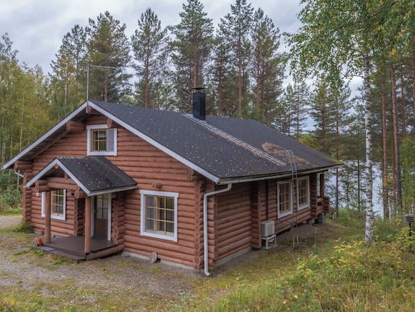 A log cabin with a chimney, a porch, and a small deck.