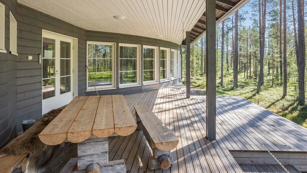A covered wooden deck with a picnic table and benches, large windows, and a forest view. - Ylläs siesta by Interhome (Ylläsjärvi)