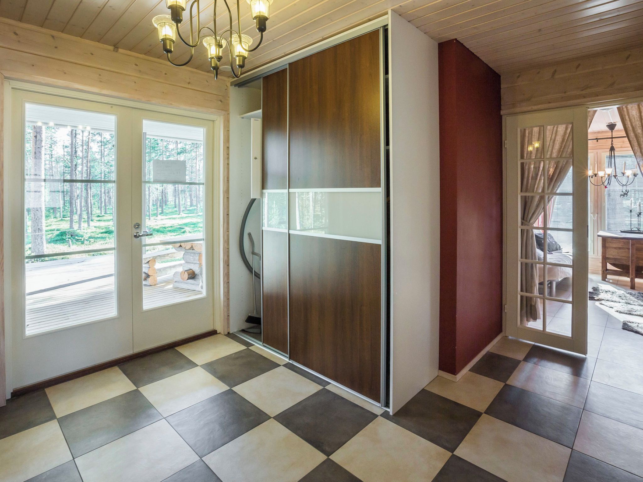 A room with a checkered floor, a sliding door, and a view of a forest through a window.