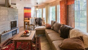 A cozy living room with a stone fireplace, a large sectional sofa, and a dining area with a wooden table and chairs. - Ylläs siesta by Interhome (Ylläsjärvi)