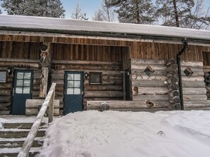 Une cabane rustique en rondins de bois, dotée de deux portes, d’une petite fenêtre et d’un escalier en bois menant à l’entrée.
