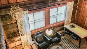 Tunnelmallinen mökin sisustus, jossa on puinen hirsiseinä, musta nahkasohva, pieni pyöreä pöytä ja siinä kulho sekä ikkuna, jossa on sälekaihtimet.