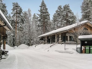 A snow-covered wooden building with a porch and steps leading up to it.