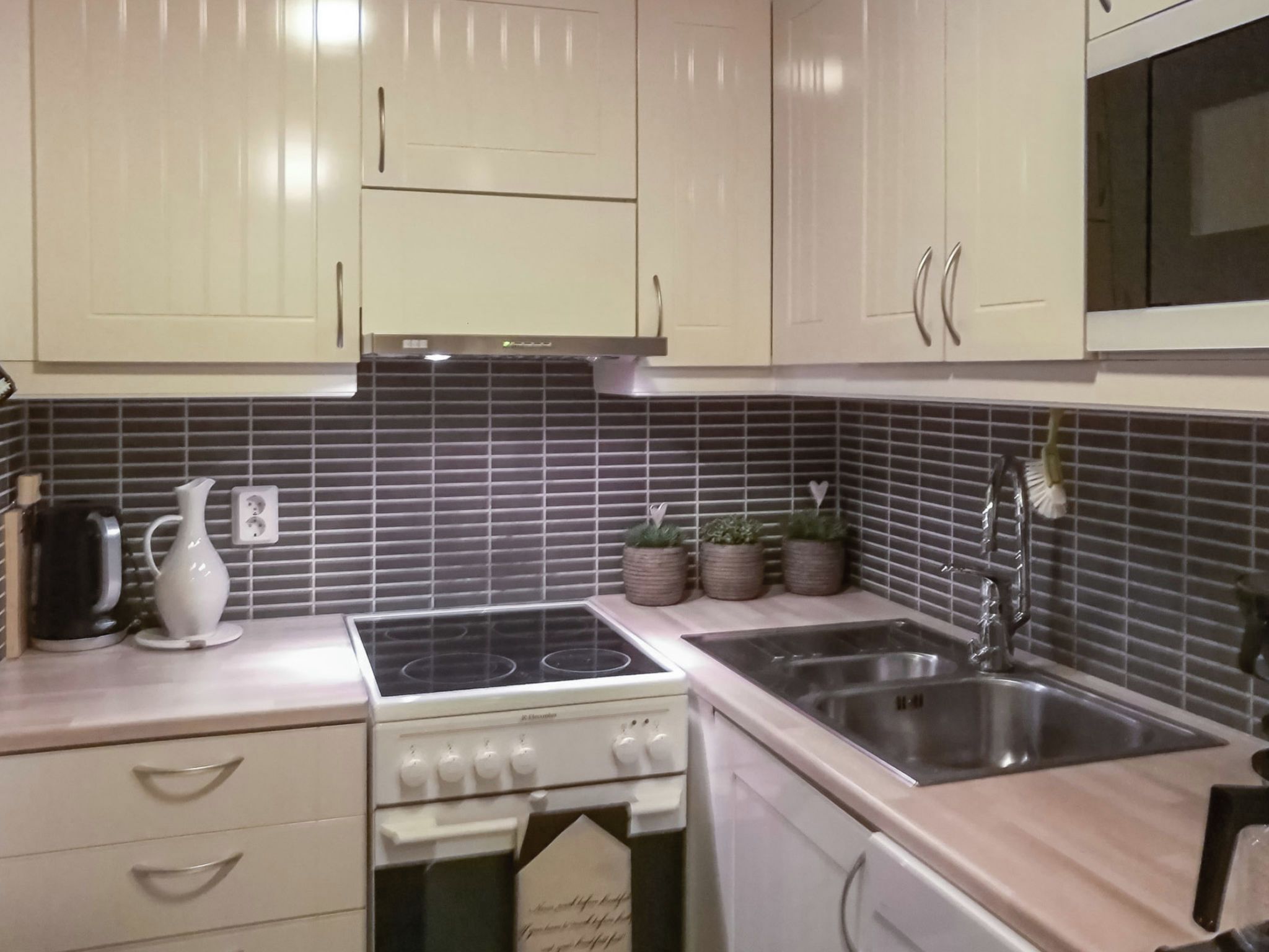 Een keuken met witte kastjes, een fornuis, een spoelbak en een magnetron.