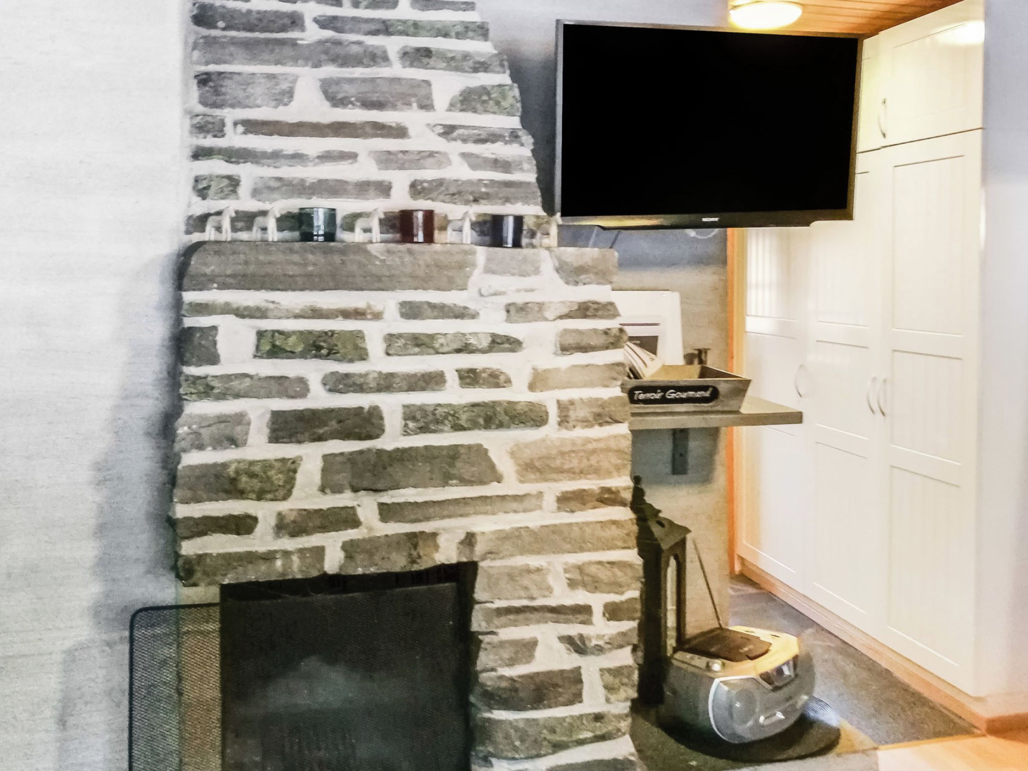 Una chimenea de piedra con un televisor montado encima, una mesita con un letrero, y un armario a la derecha.