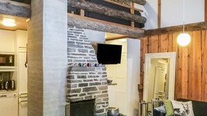 Tunnelmallinen sisustus, jossa on kivinen takka, puupalkit, taulutelevisio ja moderni keittiö.