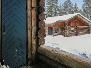 A wooden cabin with a snow-covered roof, a blue door, and a stone ledge. - Vuokatinportti b 9 by Interhome (Sotkamo)
